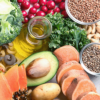 Broccoli, cherries, olive oil, grains, bread, potato, melon, pasta and avocado laid out on a wooden table