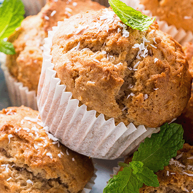 Fluffy light brown cupcakes in a white cover that only hides the base as the top protrudes out and has coconut and mint leaves sprinkled on top